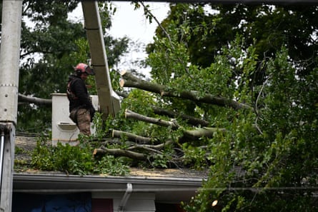 man operating machinery stands on buildingâÂÂs roof working to clear fallen trees