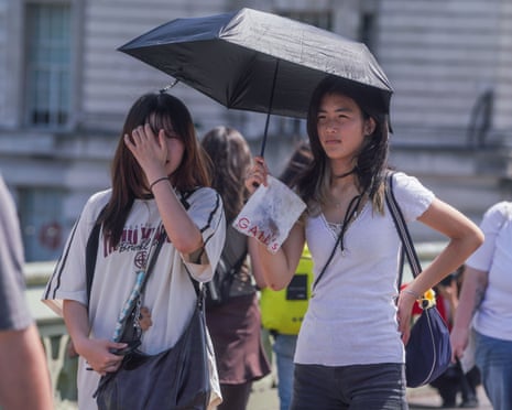 Tourists shelter under an umbrella at Westminster Bridge in London amid the extreme heat