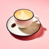 A black-rimmed white cup of frothy coffee with the foam fashioned into the shape of a cockroach, with a cockroach on a matching saucer, against a pale-pink background