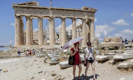 Tourists walk trough the ancient Acropolis hill, with the ruins of the Parthenon temple in the background, in Athens