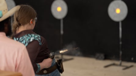 A girl wearing a brown shirt fires a gun.