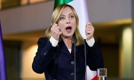 Giorgia Meloni speaking in an impassioned fashion at a lectern with both hands raised in a gesture