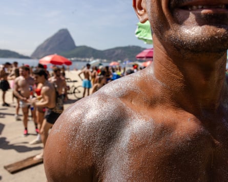 A man’s shoulder covered in silver body glitter. In the background can be seen a busy beach against the backdrop of Sugarloaf mountain.