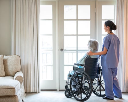 Nurse and older patient in wheelchair standing near window.
