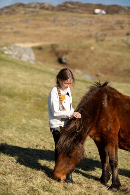 A girl pats the neck of a pony while it grazes