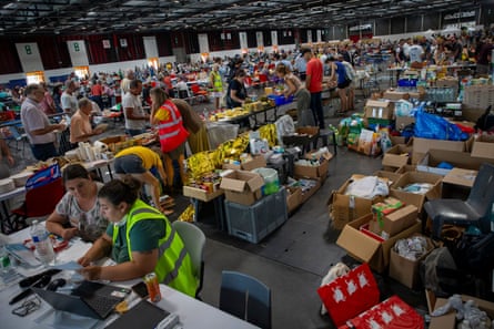 A large hall full of people, staff or volunteers wearing hi-vis and cardboard boxes of food.