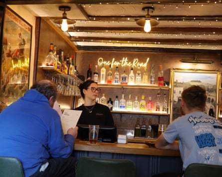 Two men sitting in stools at the bar facing a member of staff