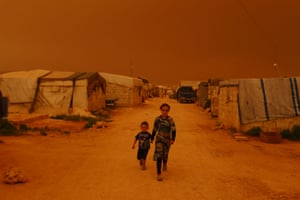 Displaced children walk past tents during a dust storm on the outskirts of the rebel-held town of Dana