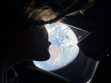 Silhouette of Christina Koch against an aerial view of Earth, from the vantage point of the interior of the Orion spacecraft