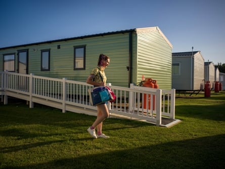 A young woman carrying bags walks past one of several long single-storey huts clad in green plastic
