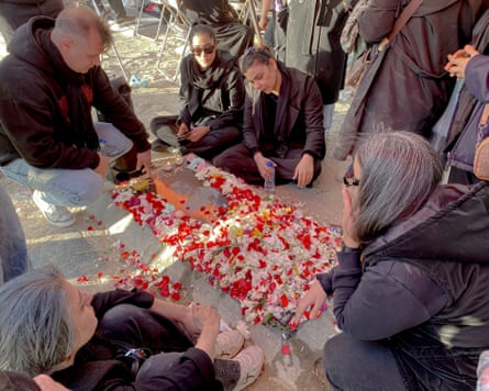 People sitting around a gravestone strewn with flowers in Behesht-e Zahra cemetery, Tehran.