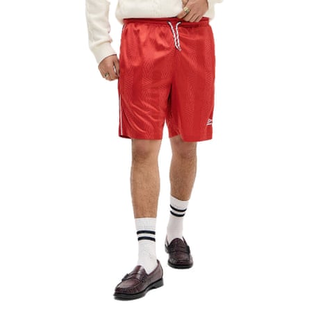 A model wears a brown chequered pair of Umbro shorts with their hands in the pockets and a thin bracelet.