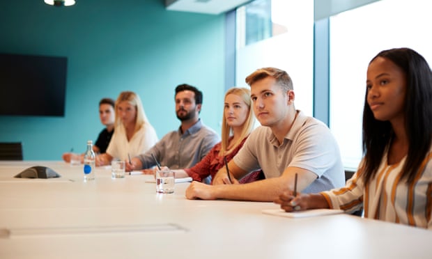 Group Of Young Candidates Sitting At Boardroom Table Listening To Presentation At Business Graduate Recruitment Assessment Day