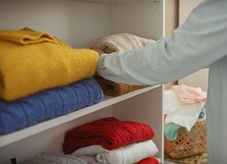 A man organising colourful sweaters in a clean, well-kept wardrobe room.