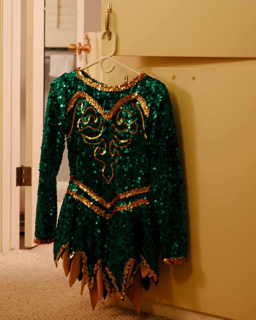 A Sun City Poms green and gold cheerleading outfit on a hanger