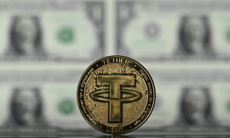 A gold-plated souvenir cryptocurrency tether coin arranged beside a screen displaying US dollar notes