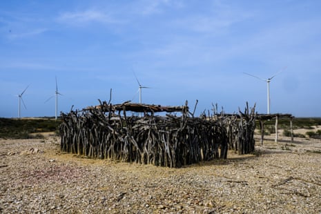 Four wind turbines next to an ancestral graveyard of the Wayúu people built of unshaped branches.