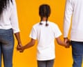 Little girl holding hands of her adoptive parents, rear view.