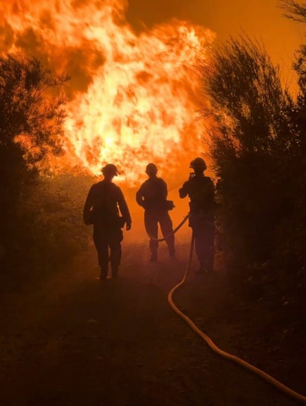 three firefighters are silhouette by a fire