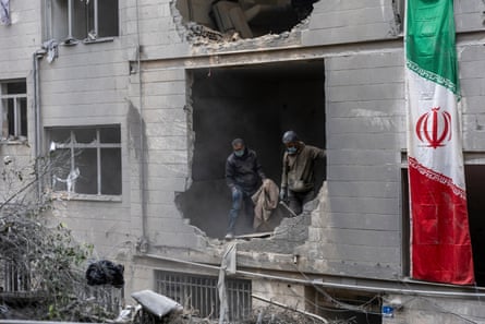 Two men dispose of rubble through the gaping hole in the front wall of the building. An Iranian flag hangs to the side the building