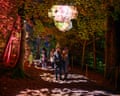 A couple gazes up at a glowing cloud-like light installation above a woodland path at night