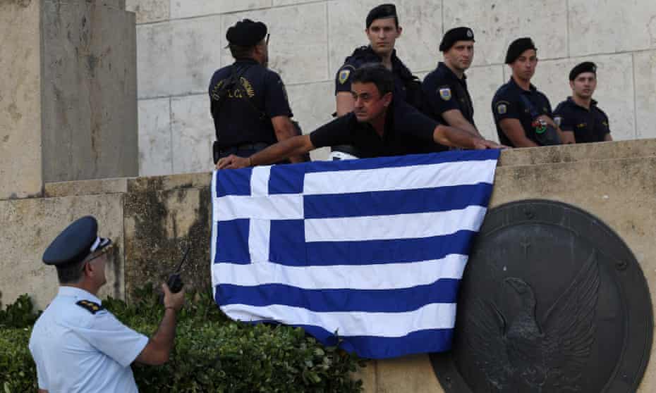 An anti-austerity protester places a Greek flag next to an entrance to the Greek parliament