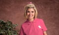 Emma Barnett wearing a bright pink polo top, standing next to a plant against a mottled brown wall