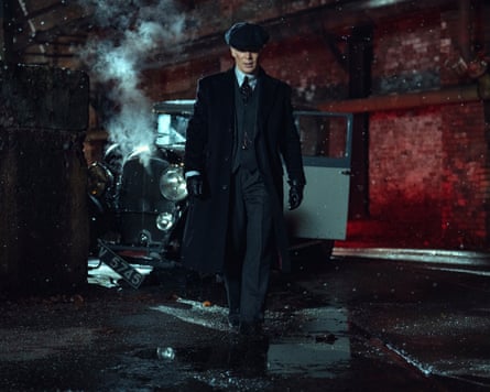 Cillian Murphy in cap and suit walking at night in front of a vintage car