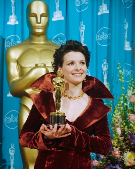 Woman in burnt orange velvet dress smiles while holding Oscar statuette