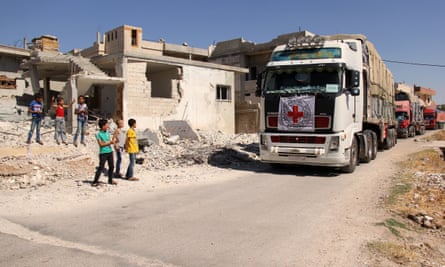 Syrian children watch aid trucks drive through a village