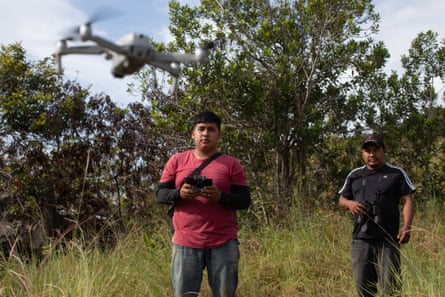 Two Indigenous men fly a drone camera in a forested area
