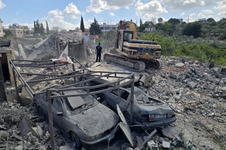 एक आदमी एक नष्ट हुई इमारत के धू-धू कर जलते मलबे के बीच खड़ा है।