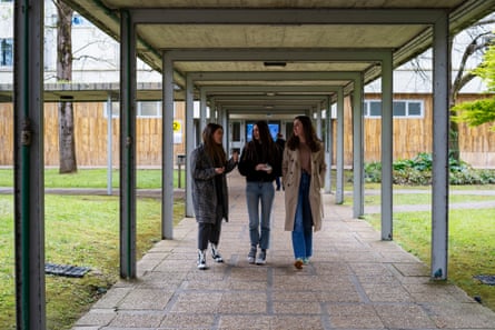 Three young women walking along a walkway with a roof.