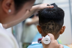 A barber shaves a tank design into the back of a child's haircut