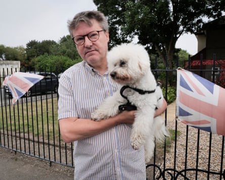 A man holds his bichon frisé standing by railings with union flags attached