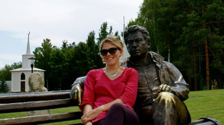 A woman sitting on a bench next to a seated statue of a man