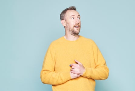 A portrait of Alex Horne wearing a yellow jumper