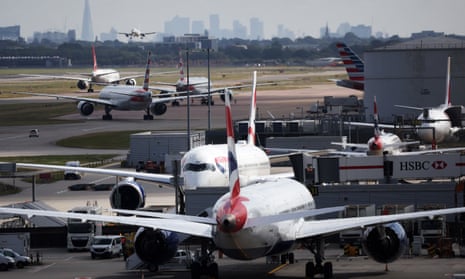 view of planes on their stands and taxiing out to the runway in a queue at Heathrow, with one plane coming in to land and the London skyline seen in the background