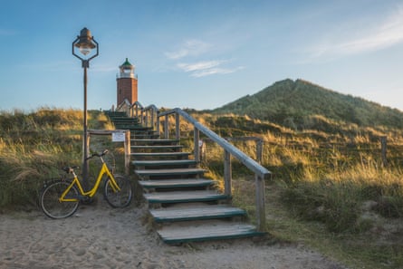 Parked bike on beach next to steps and lighthouse with sand dunes around