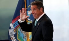 Andrew Cuomo smiles and waves with the New York state flag behind  him.