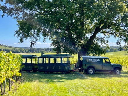 A Land Rover pulls a train of carriages through sunny vineyards