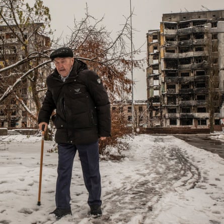 An elderly man walks past the snow-covered rubble of a residential building in Borodianka