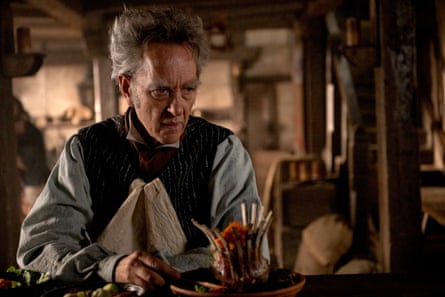 A man with grey hair sitting at a table creating something made out of wicker