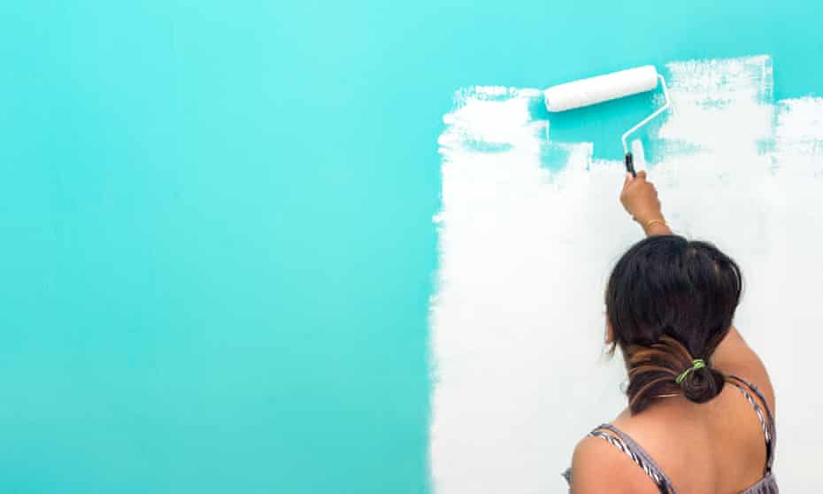 A young woman painting a wall with a paint roller.