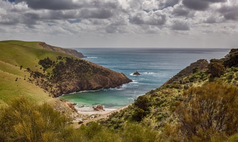 View of a beautiful uninhabited cove surrounded by green-clad cliffs under a sky with dramatic clouds