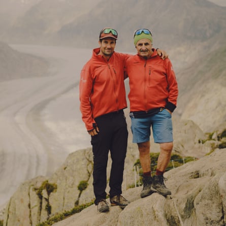 Portrait of an older man and a younger one with their arms around each other and the glacier behind them