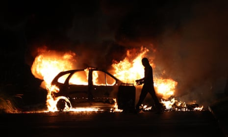 A man walks in front of a car set ablaze amid the unrest.