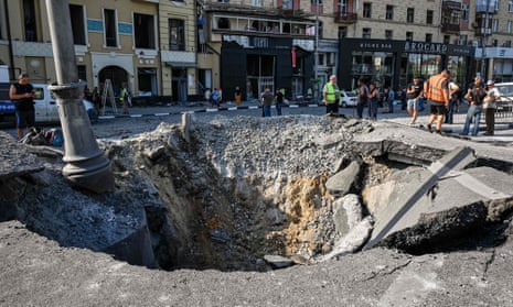 Municipal workers stand around a crater in a road  after an overnight missile strike in Kharkiv, Ukraine