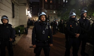 Nighttime view of police in helmets and riot gear on urban street.