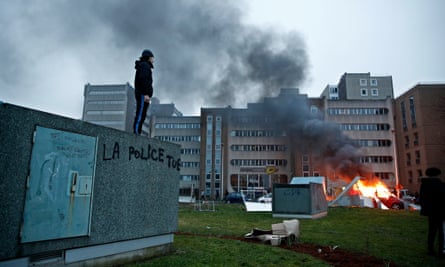 A man stands on a wall with a slogan reading: ‘Police kills’ next to a burning car in Bobigny riots